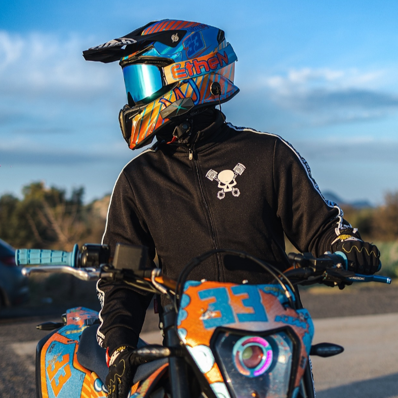 Motocross rider in colorful helmet and black jacket sitting on dirt bike