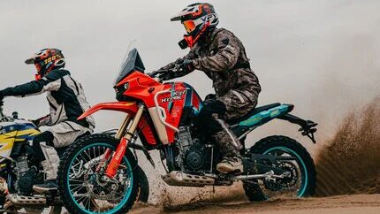 Two motorcyclists racing across desert dunes, showcasing durable riding gear and off-road bikes in action.