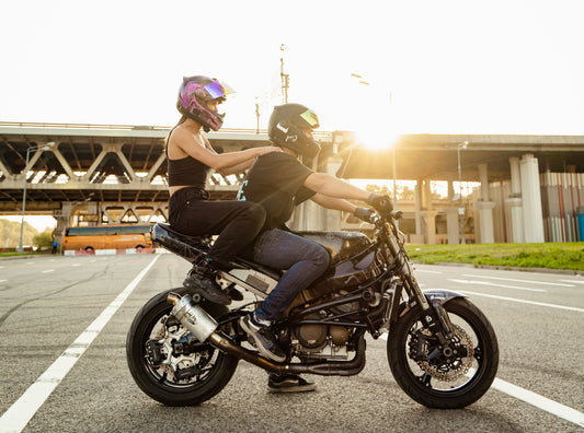 Two people riding a black motorcycle on a city street at sunset blog cover