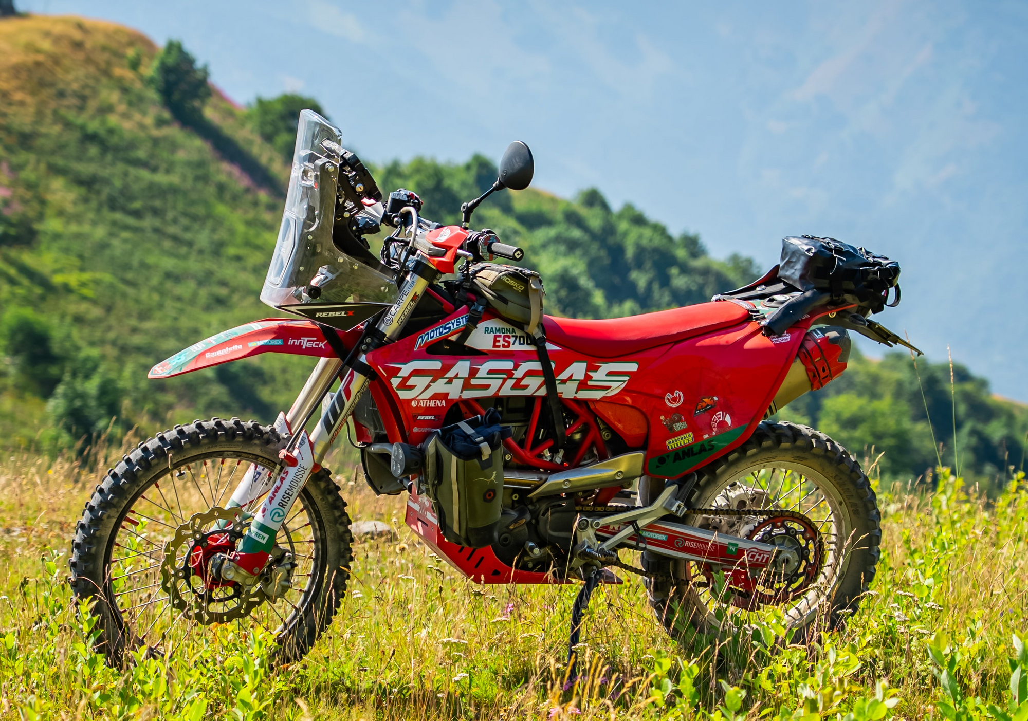 Red GasGas off-road motorcycle parked in a grassy field against cloudy mountain peaks blog cover