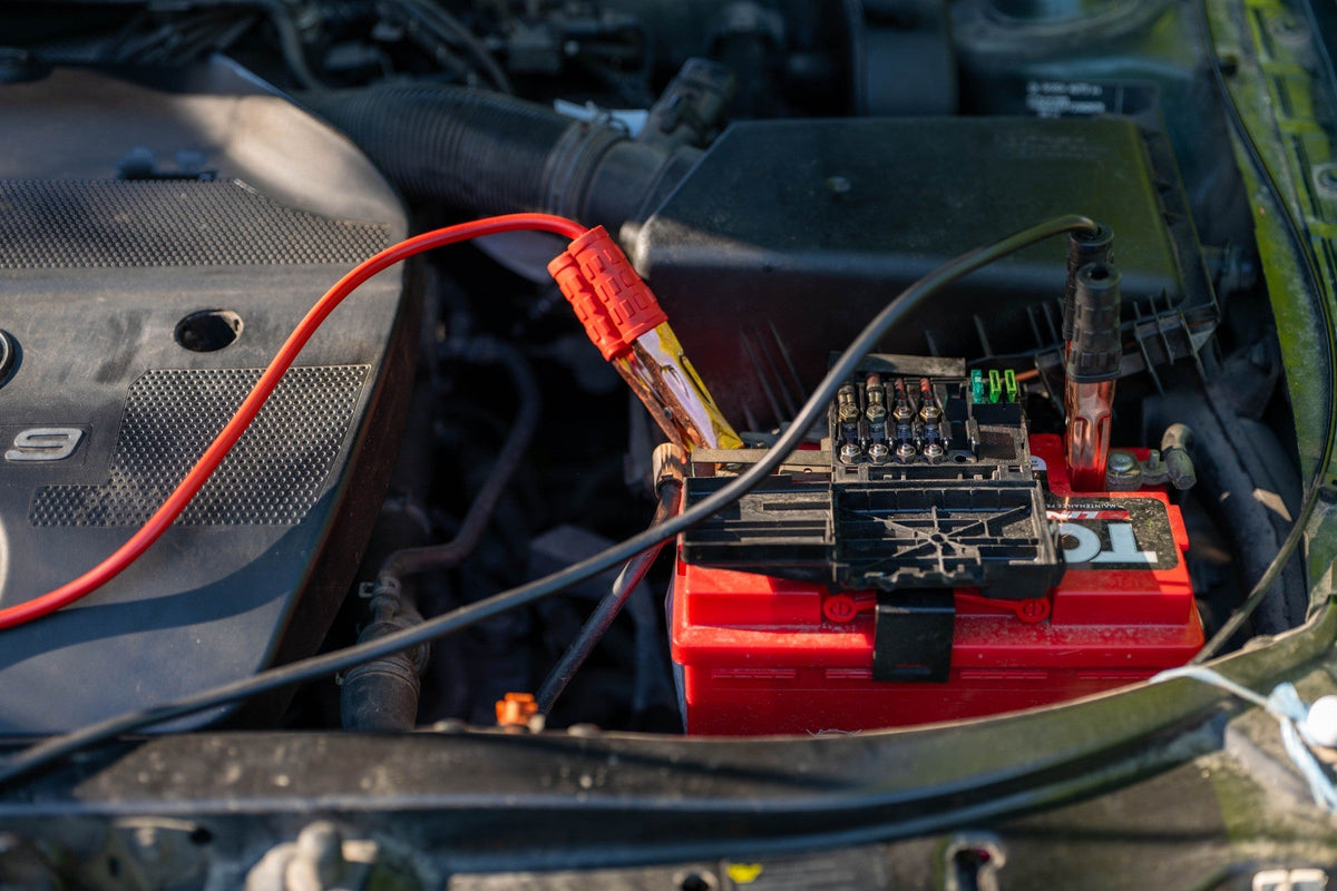Jumper cable clamp connected to a red car battery in the engine bay blog cover