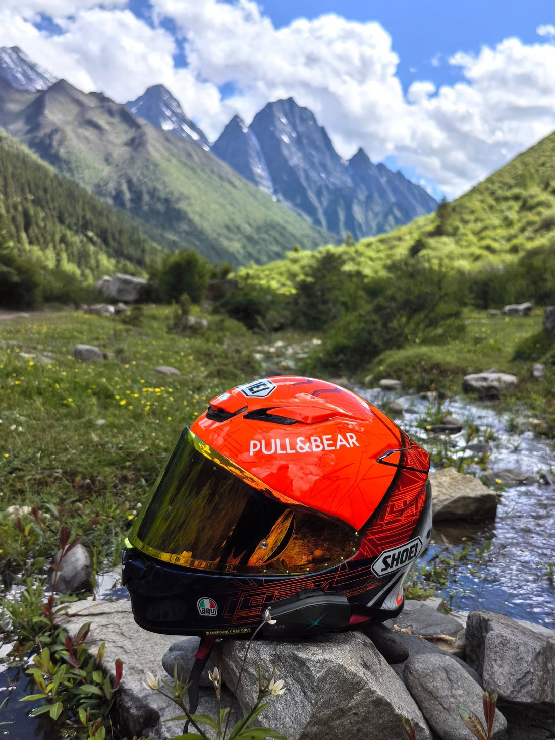 Orange motorcycle helmet resting on a river rock with snowy mountain scenery blog cover