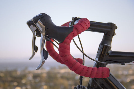 Close-up of a road bicycle drop handlebar with red bar tape and brake levers blog cover