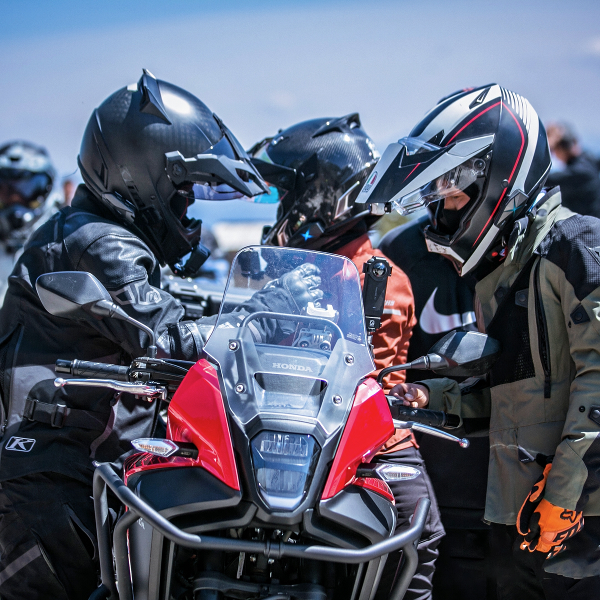Group of adventure motorcyclists discussing routes beside touring motorcycle wearing helmet mesh intercoms